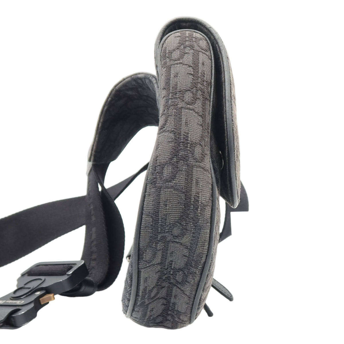 A close-up of a black shoulder bag with a textured, embossed monogram pattern, showing the strap and side profile against a white background.