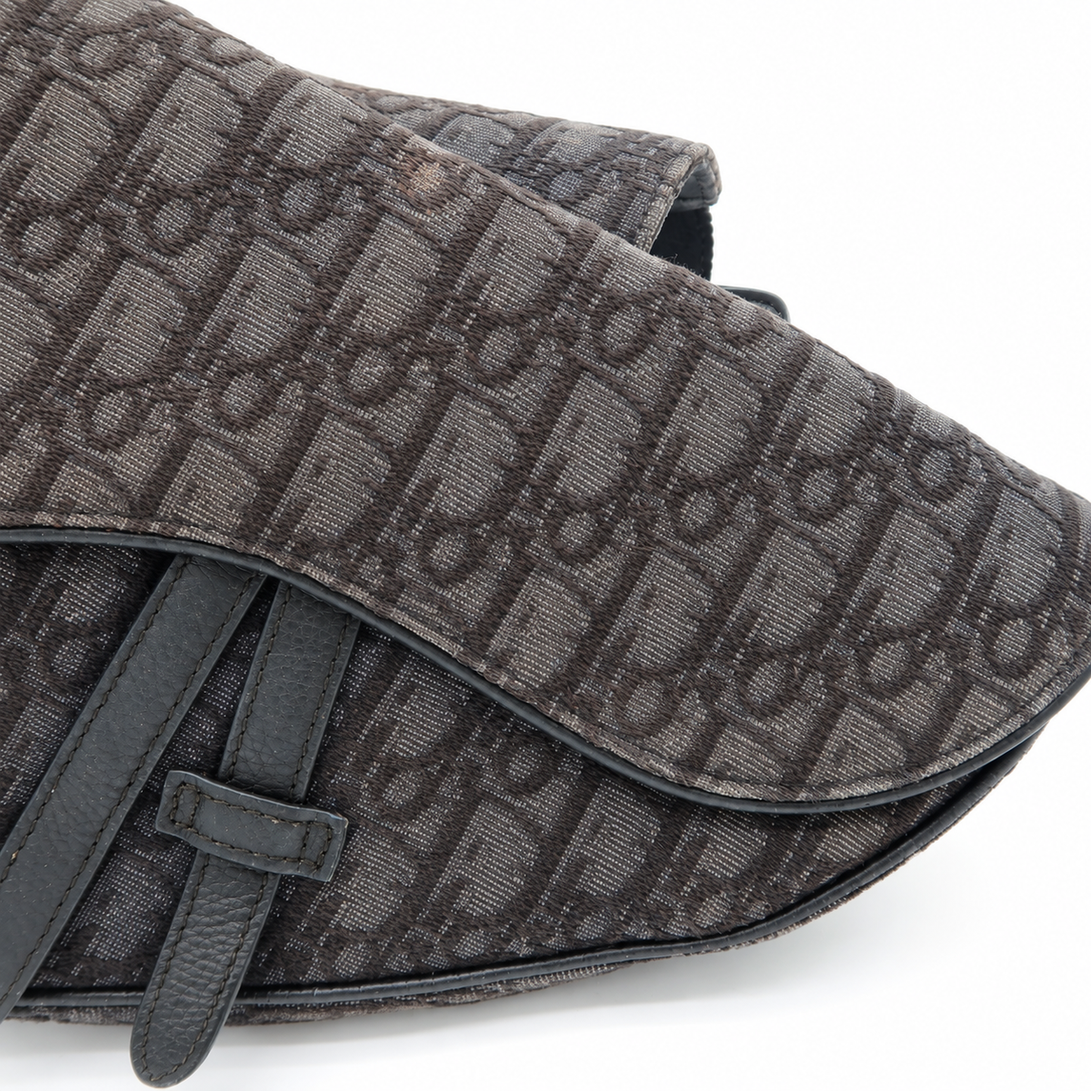Close-up of a dark brown Dior Oblique coated canvas bag with a dark brown leather strap and trim, set against a plain white background.