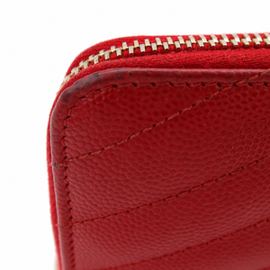 Close-up of a red pebbled leather zip-around wallet showing the texture, stitching, and a gold-tone zipper on a white background.