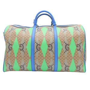 A Gucci duffle bag featuring a green and beige argyle pattern with brown interlocking G logos, accented by bright blue leather handles and trim, set against a plain white background.