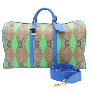 A Gucci duffle bag in brown GG Supreme monogram canvas with bright green and blue diamond pattern panels, featuring blue leather handles and a matching blue detachable shoulder strap on a white background.