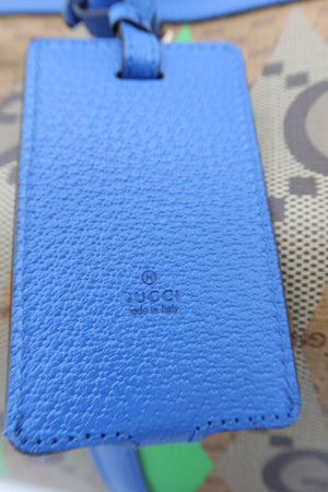 A close-up of a blue textured leather luggage tag with a debossed 'GUCCI made in Italy' logo, resting on a patterned Gucci canvas surface.
