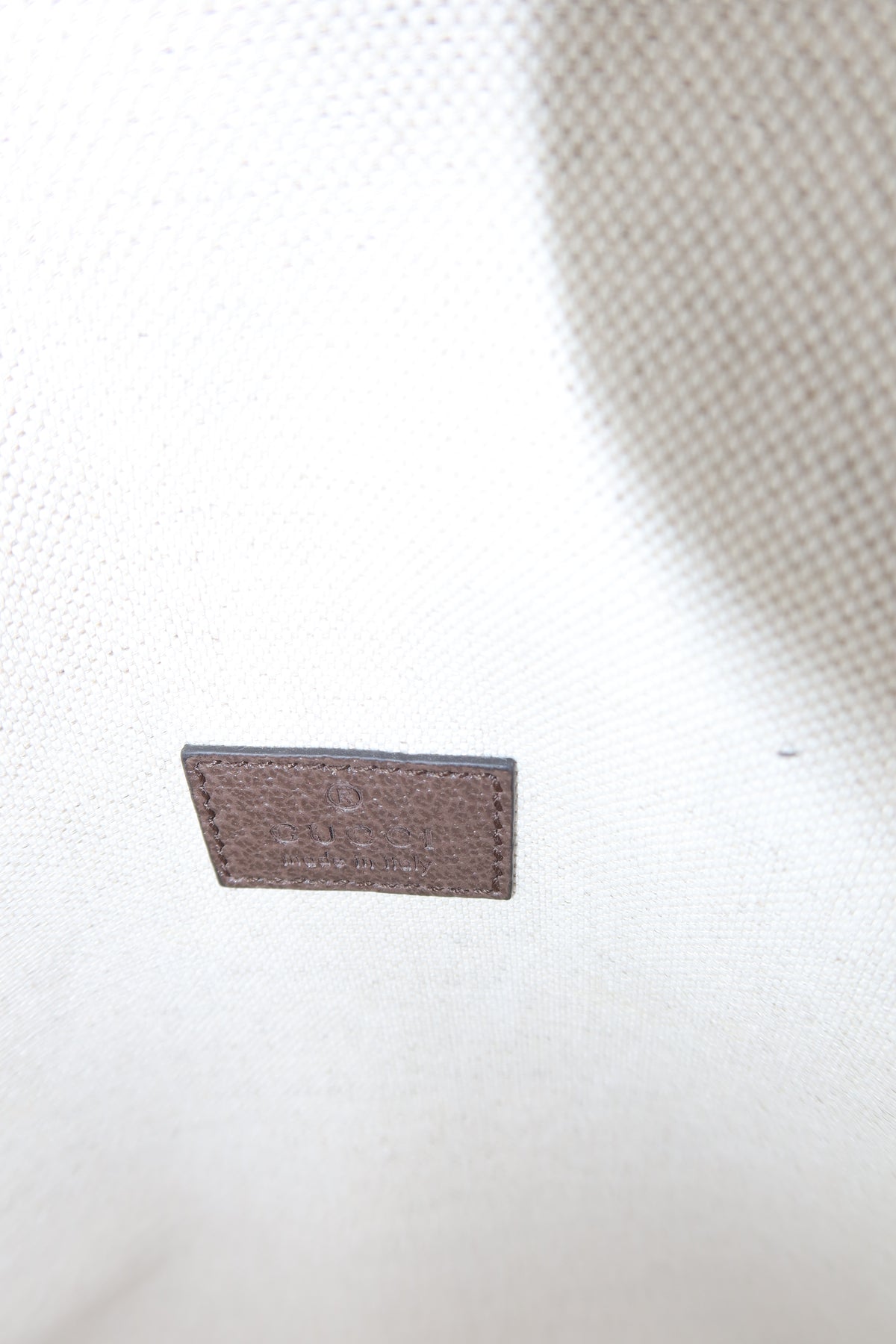 A small rectangular brown leather brand patch sewn onto a white canvas fabric surface.