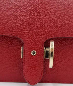 Close-up of a red pebbled leather handbag featuring a front flap with a gold-tone turn-lock clasp and a central rivet.