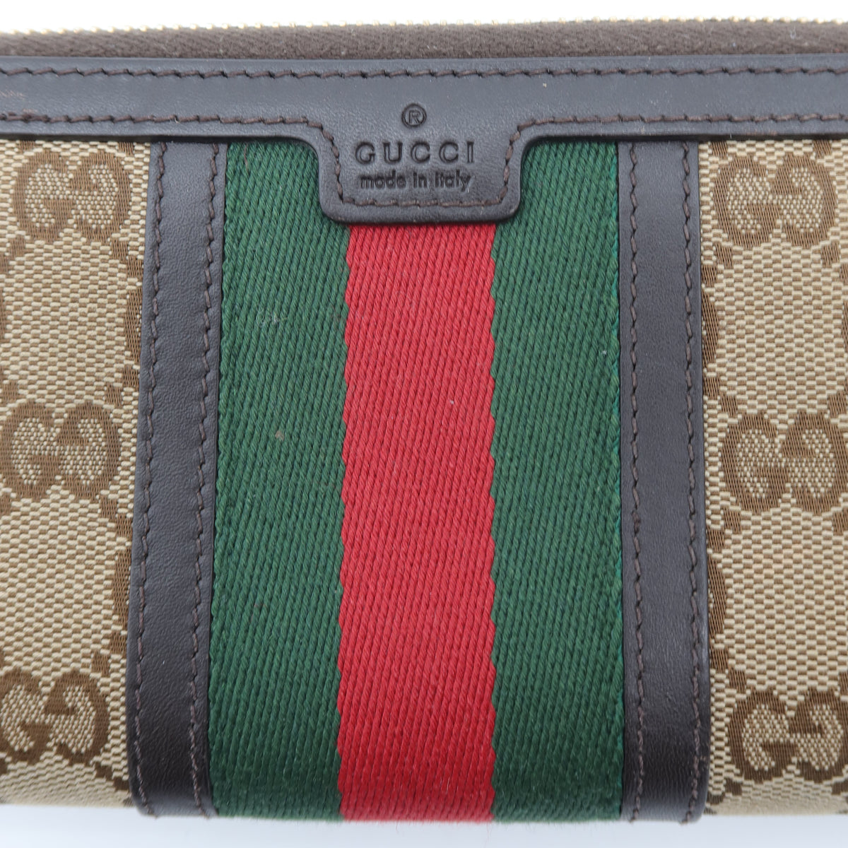 Gucci monogram canvas zip-around wallet with green and red web stripe and dark brown leather trim, featuring a central Gucci logo plaque.