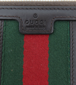 Close-up of a Gucci wallet showing the iconic green and red web stripe pattern with dark brown leather trim and a central embossed Gucci logo patch.