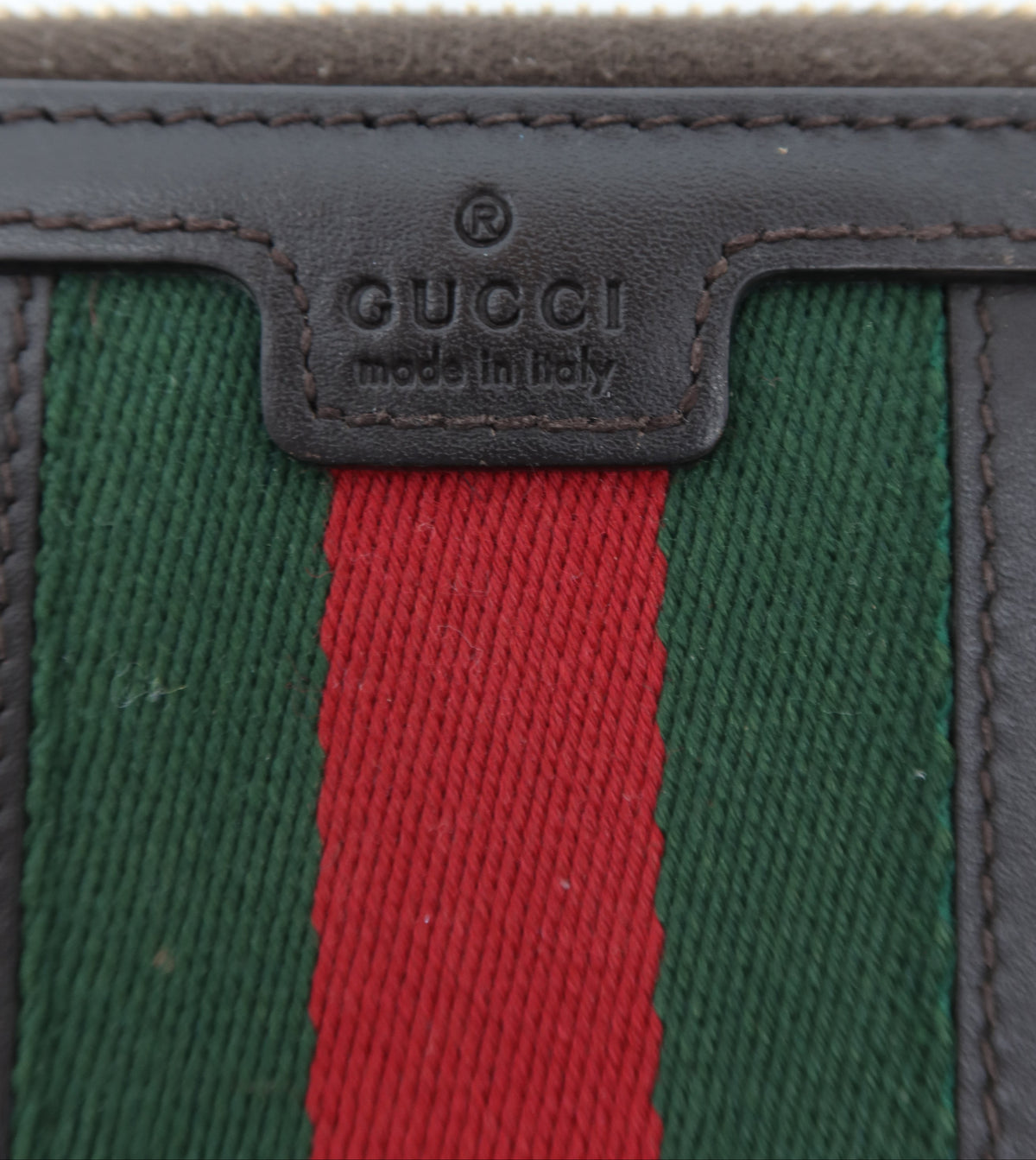 Close-up of a Gucci wallet showing the iconic green and red web stripe pattern with dark brown leather trim and a central embossed Gucci logo patch.