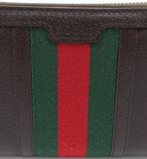 Close-up of a brown leather wallet featuring the signature green and red web stripe pattern on the front, with a subtle embossed Gucci logo on the leather tab above the stripes.