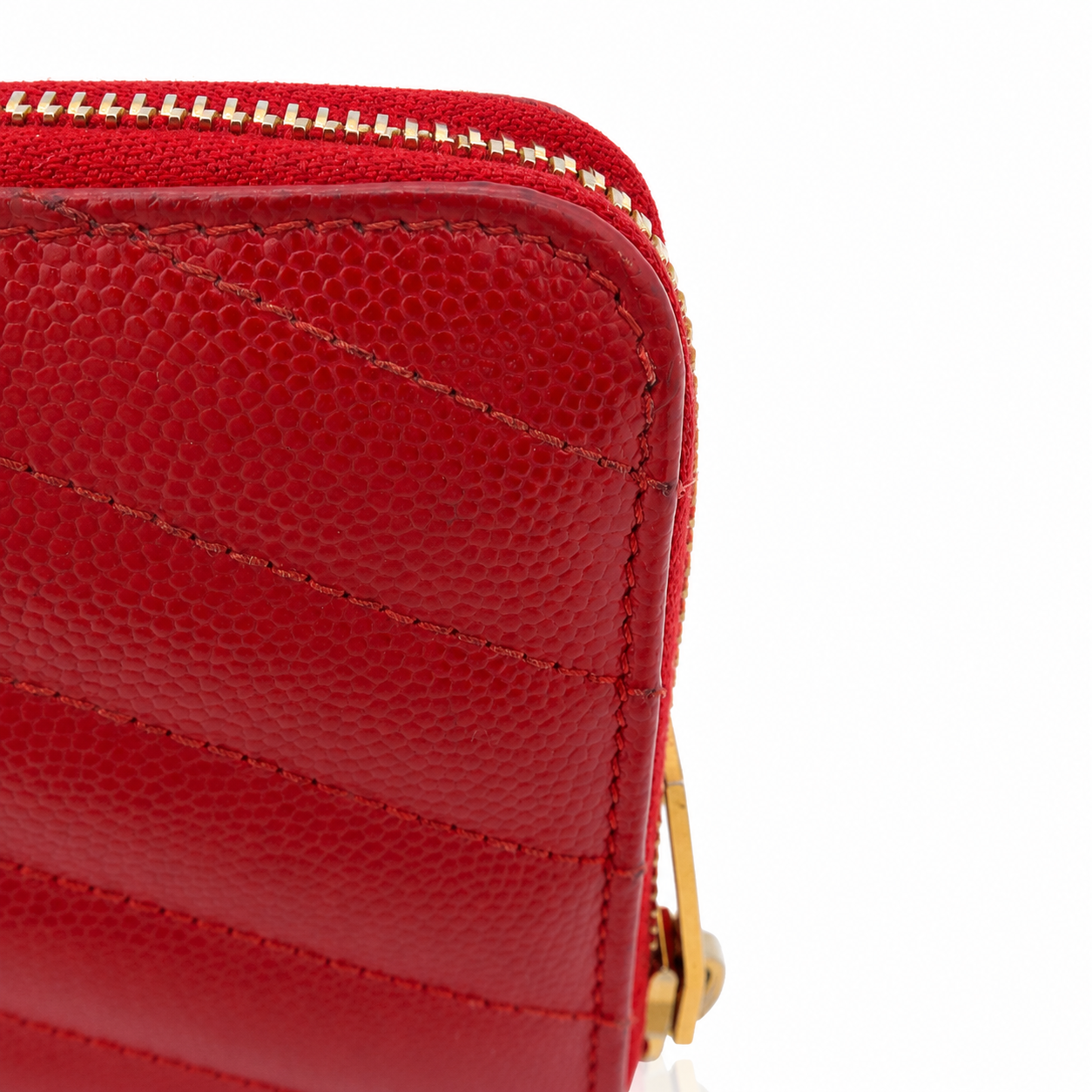 Close-up of a red pebbled leather zip-around wallet or clutch with gold-tone zipper teeth and a small gold hardware accent on a white background.