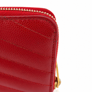 Close-up of a red pebbled leather zip-around wallet or clutch with gold-tone zipper teeth and a small gold hardware accent on a white background.