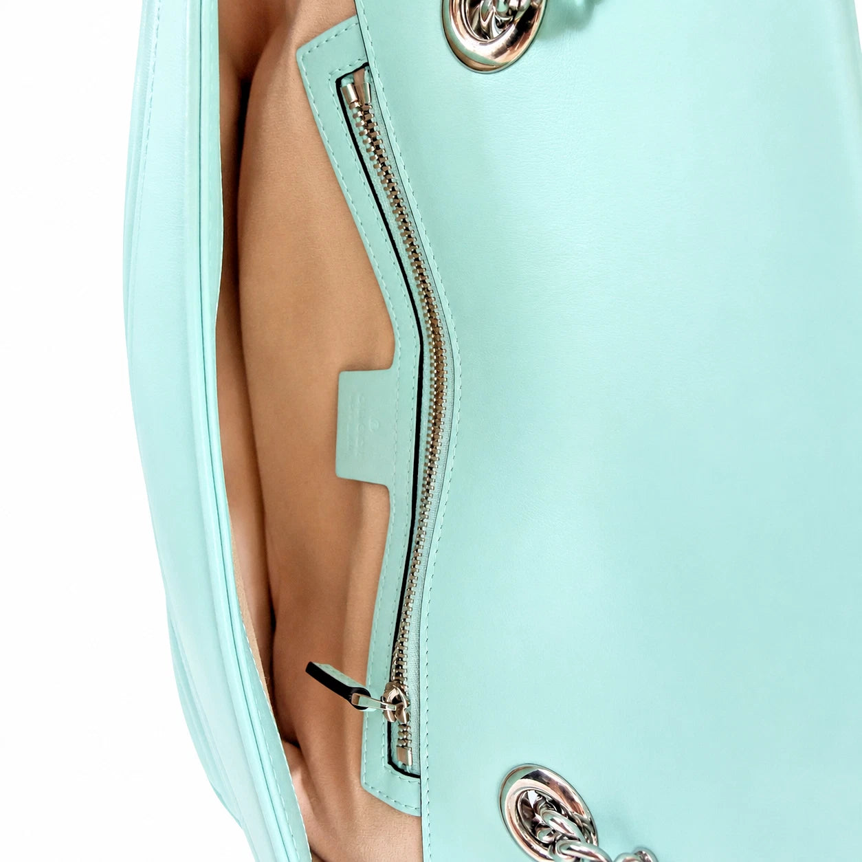 Close-up of a mint green leather handbag showing the interior lining, a zippered pocket, and silver-tone hardware against a white background.