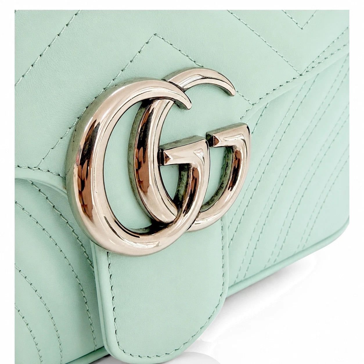 A close-up of a mint green quilted leather handbag featuring a polished gold-tone interlocking GG logo clasp, representing the Gucci brand.
